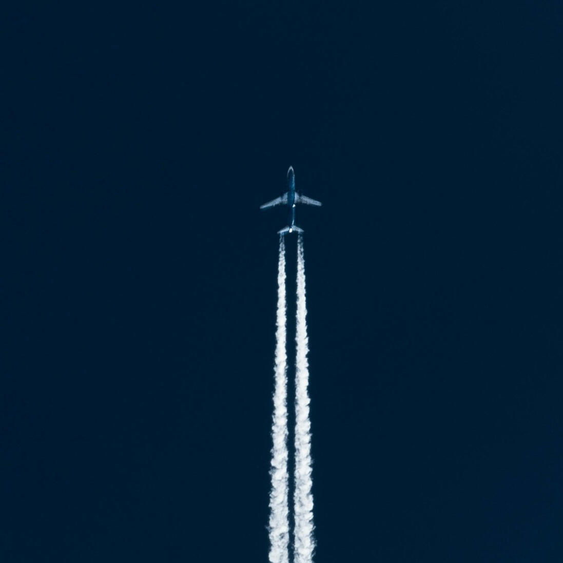 Website Launch Airplane flying through a clear sky with white contrails behind it.