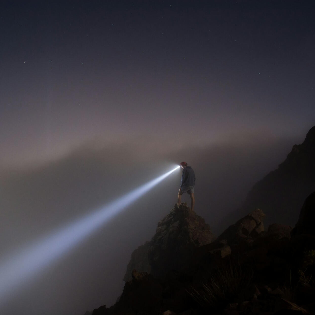 Discovery & Strategy Climber standing on a mountain summit at night, using a headlamp to illuminate the path ahead.